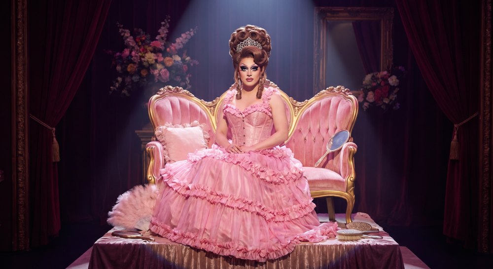gemini-3-pro generation: a person in a pink corseted ball gown and tiara seated on a pink throne, surrounded by pink props under a dramatic spotlight